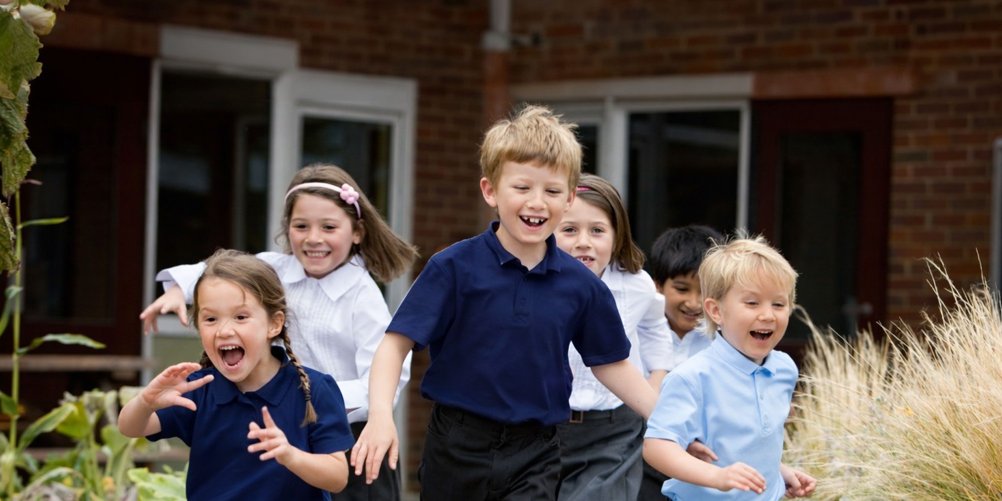 Students running and smiling outside the school building.