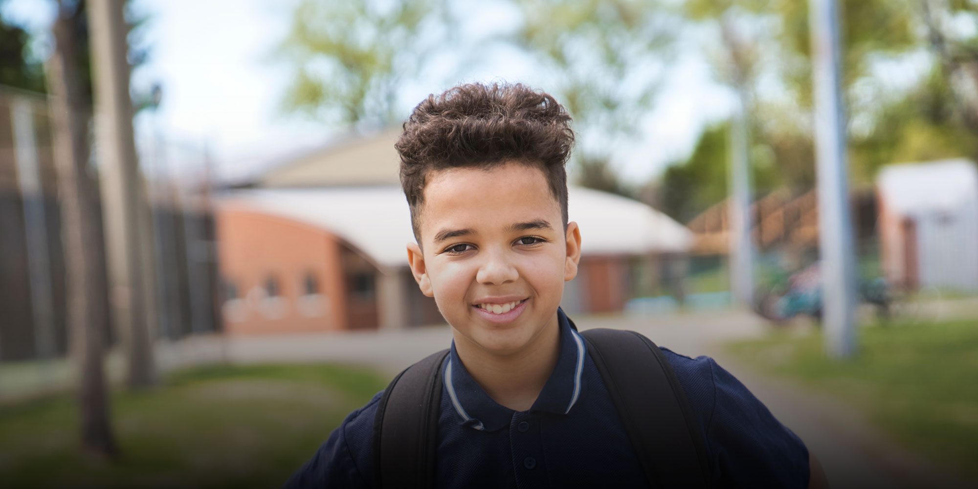 Smiling student with a backpack standing outside.