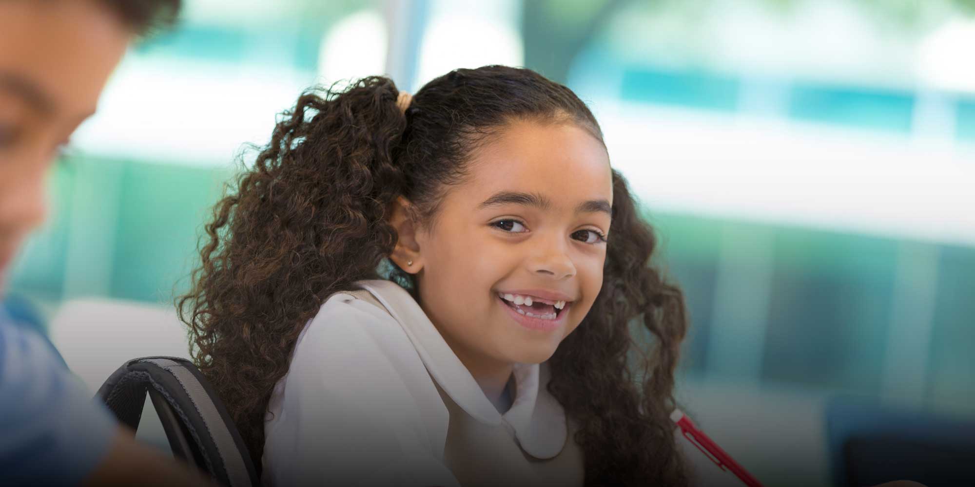 Smiling student holding a red pencil in a classroom.